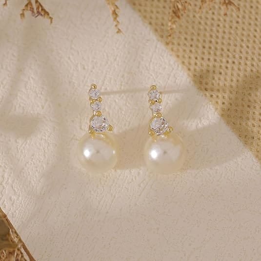 Pearl earrings featuring a round white pearl and three small cubic zirconia stones in a gold-toned vertical setting