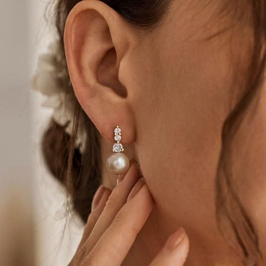 Pearl drop earring with three small sparkling stones set in gold, worn on a person's ear