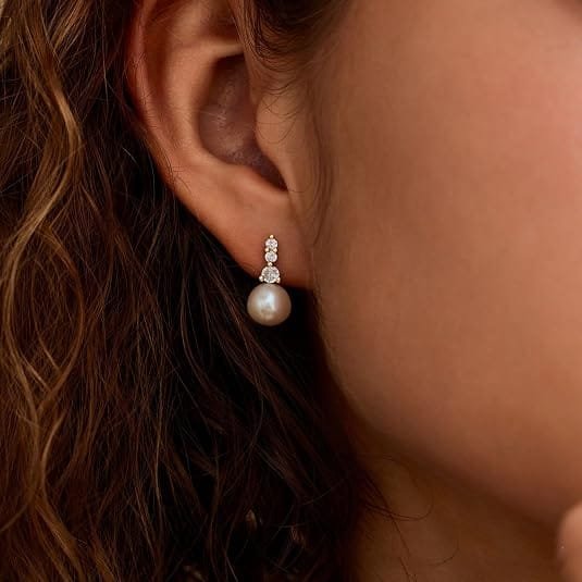 White pearl earring with three small sparkling stones worn on an ear